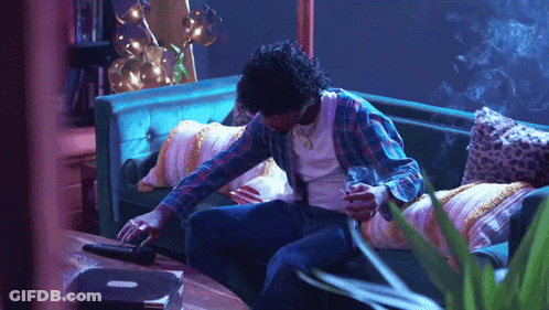 A Man Sitting On A Couch Smoking A Cigarette And Looking At His Phone GIF