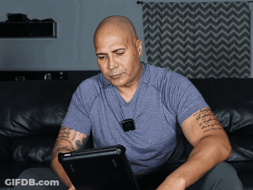 A Man Sitting On A Couch Using A Laptop With A Tattoo On His Arm GIF