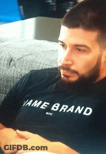 A Man Sitting On A Couch Wearing A Black Shirt That Says Name Brand Nyc GIF