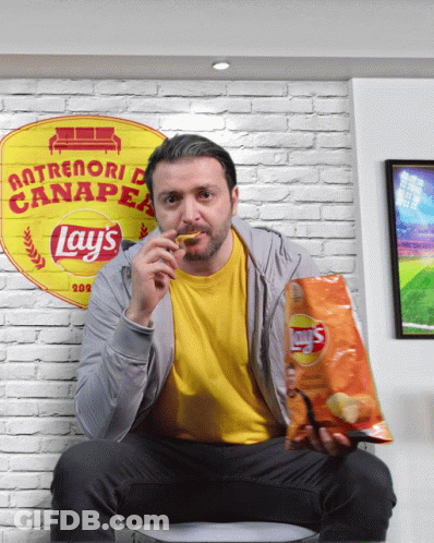 A Man Sitting On A Couch With A Bag Of Lays Chips GIF