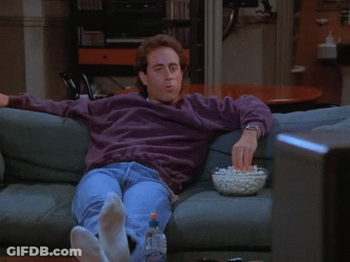 A Man Sitting On A Couch With A Bowl Of Popcorn In Front Of Him GIF