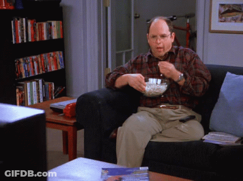 A Man Sitting On A Couch With A Bowl Of Popcorn In His Hand GIF