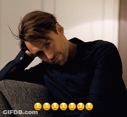 A Man Sitting On A Couch With A Bunch Of Smiley Faces Behind Him GIF