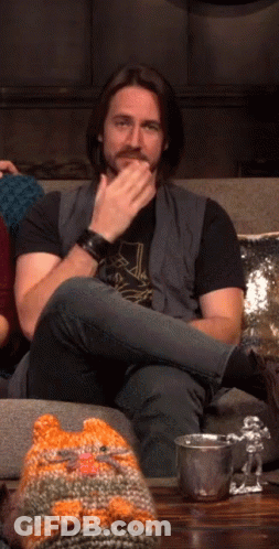A Man Sitting On A Couch With A Knitted Cat Hat GIF