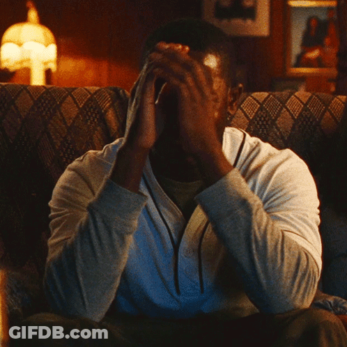A Man Sitting On A Couch With His Hand On His Face GIF