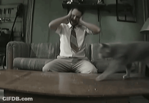 A Man Sitting On A Couch With His Hands On His Head GIF