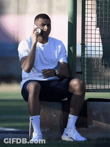 A Man Sitting On A Ledge Talking On A Cellphone GIF