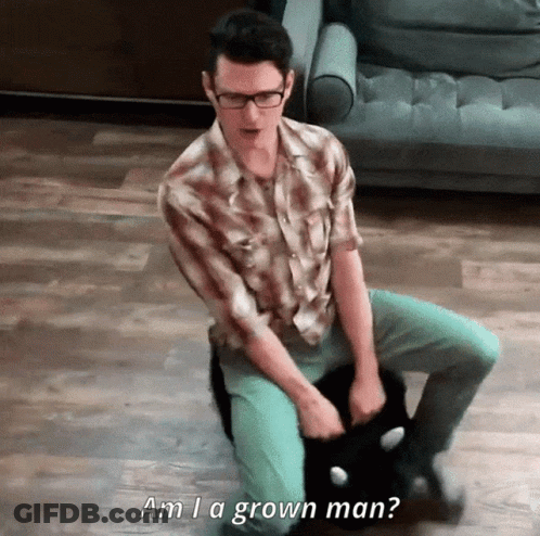 A Man Sitting On The Floor Holding A Cat With The Words Am I A Grown Man Written Below Him GIF