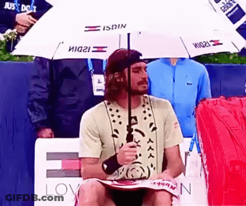 A Man Sitting Under An Umbrella That Says Isdin On It GIF