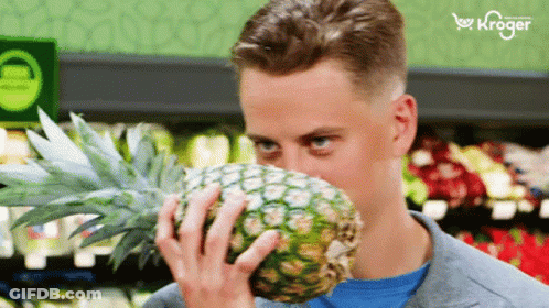 A Man Smells A Pineapple In A Grocery Store With A Kroger Logo In The Background GIF