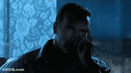 A Man Smoking A Cigarette In A Dark Room With A Blue Background GIF