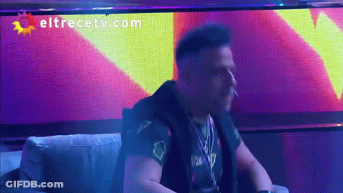 A Man Smoking A Cigarette In Front Of A Eltrecetv.com Sign GIF