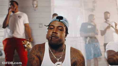 A Man Smoking A Cigarette In Front Of A Group Of Men GIF