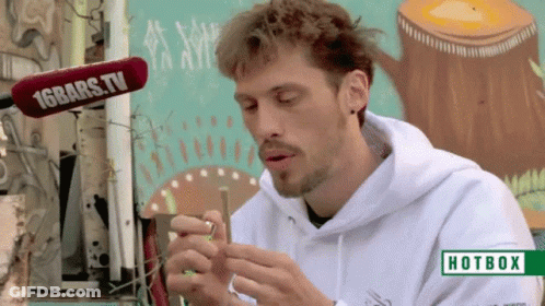 A Man Smoking A Cigarette In Front Of A Hotbox Sign GIF