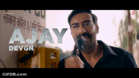 A Man Smoking A Cigarette In Front Of A Sign That Says A Jay Devgn GIF