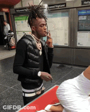 A Man Smoking A Cigarette In Front Of A Sign That Says Hollywood / Highland GIF