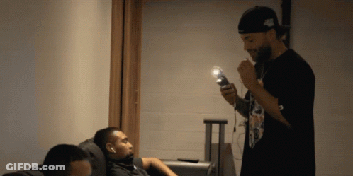 A Man Smoking A Cigarette While Another Man Sits On The Couch GIF