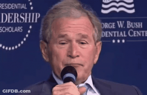 A Man Speaking Into A Microphone In Front Of A Sign That Says George W. Bush Presidential Center GIF