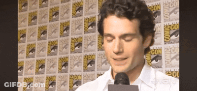 A Man Speaking Into A Microphone In Front Of A Wall That Says Comic Con On It GIF