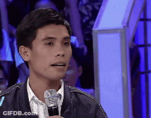 A Man Speaking Into A Microphone With A Crowd Behind Him GIF