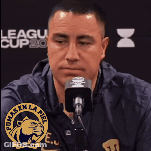 A Man Speaking Into A Microphone With A Pumas En La Piel Logo On His Shirt GIF