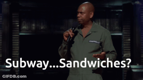 A Man Speaking Into A Microphone With The Words " Subway Sandwiches " Behind Him GIF