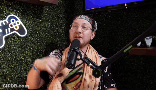 A Man Speaking Into A Shure Microphone In Front Of A Video Game Controller Sign GIF