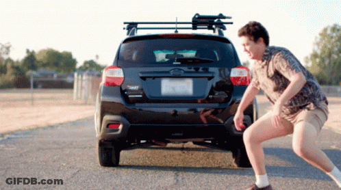 A Man Squats In Front Of A Black Subaru GIF