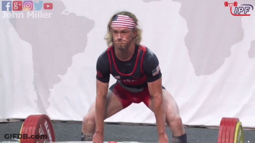 A Man Squatting Down With A Barbell In Front Of A Sign That Says John Miller GIF