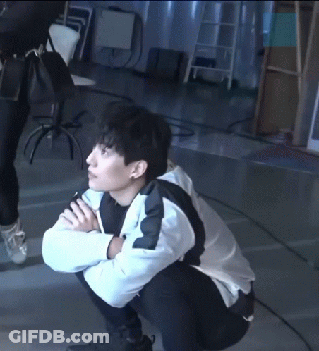 A Man Squatting Down With His Hands Folded GIF