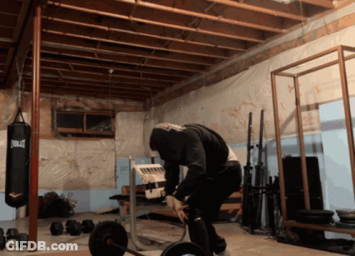 A Man Squatting In A Gym With A Everlast Punching Bag In The Background GIF