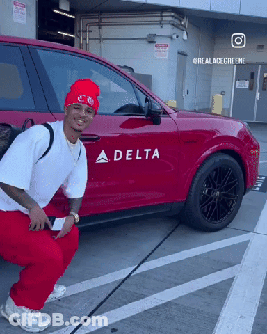 A Man Squatting In Front Of A Red Car That Says Delta GIF
