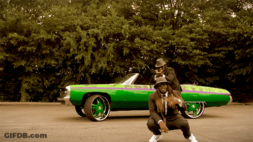 A Man Squatting Next To A Green Car With A Purple Stripe GIF