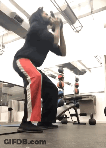 A Man Squatting With A Dumbbell In His Mouth GIF