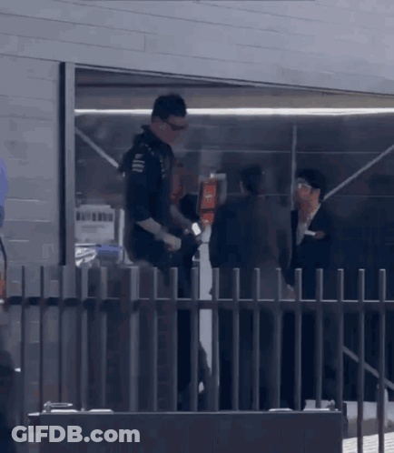 A Man Standing Behind A Fence Talking To A Man In A Suit GIF