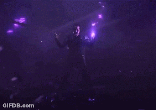 A Man Standing In A Dark Room With Purple Lights Around Him GIF