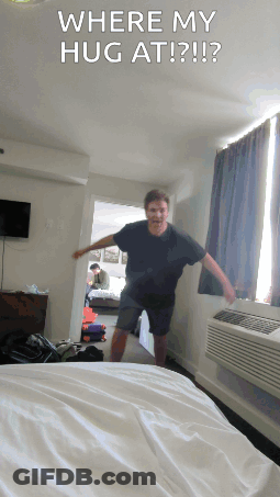 A Man Standing In A Hotel Room With The Words " Where My Hug At " On The Bottom GIF