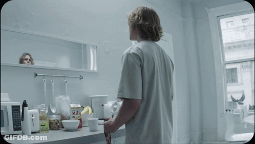 A Man Standing In A Kitchen Looking At A Box Of Milk GIF