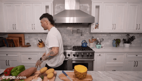 A Man Standing In A Kitchen With A Pineapple Sliced In Half On A Cutting Board GIF