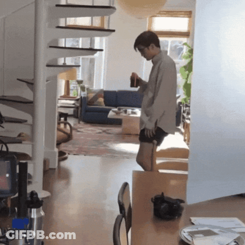 A Man Standing In A Living Room Holding A Bottle GIF