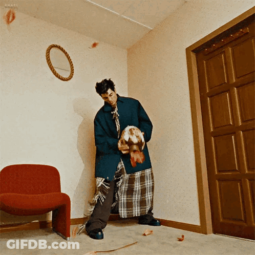 A Man Standing In A Room With A Red Chair And A Mirror On The Wall GIF