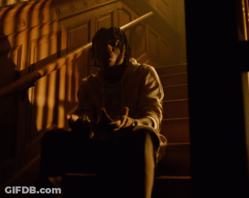 A Man Standing In A Room With White Curtains And A Necklace With The Letter O On It GIF