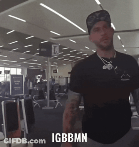A Man Standing In An Airport With Igbbmn Written On The Bottom Of His Shirt GIF