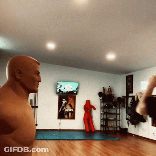 A Man Standing In Front Of A Boxing Dummy In A Room GIF