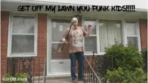 A Man Standing In Front Of A Brick House With The Words Get Off My Lawn You Punk Kids Written Above Him GIF
