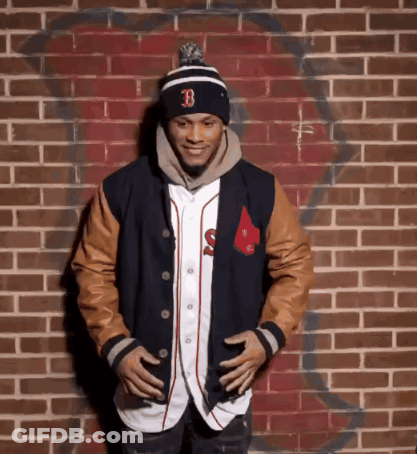 A Man Standing In Front Of A Brick Wall Wearing A Hat With The Letter B On It GIF