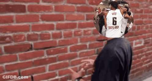 A Man Standing In Front Of A Brick Wall With A Picture Of A Man Wearing A Jersey With The Number 6 On It GIF