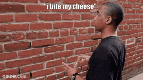 A Man Standing In Front Of A Brick Wall With The Words " I Bite My Cheese " Above Him GIF