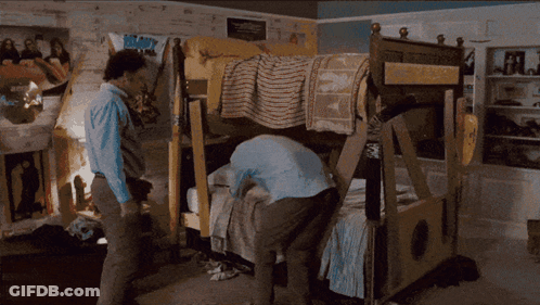 A Man Standing In Front Of A Bunk Bed With A Poster On The Wall That Says ' Boom ! ' GIF