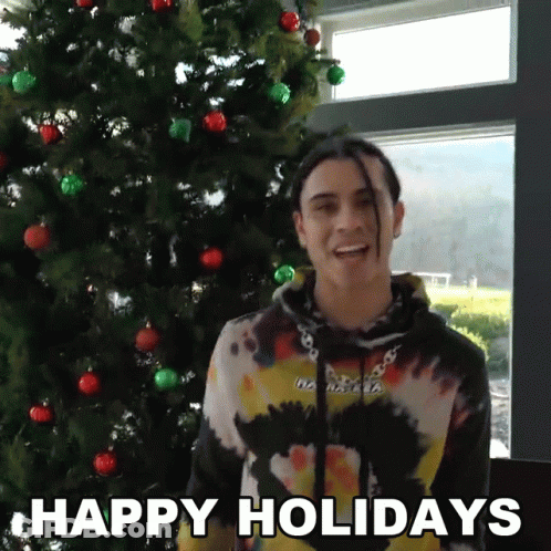 A Man Standing In Front Of A Christmas Tree With The Words Happy Holidays On The Bottom GIF
